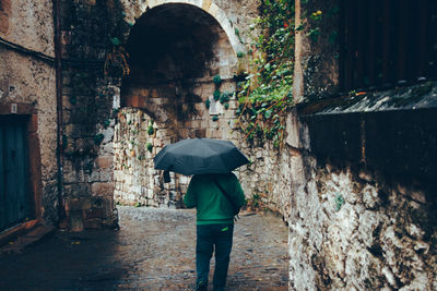 Rear view of man walking on wet street during rainy season