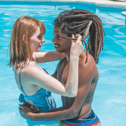 Interracial couple in the pool hugging and looking at each other
