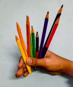 Close-up of hand holding colored pencils against white background