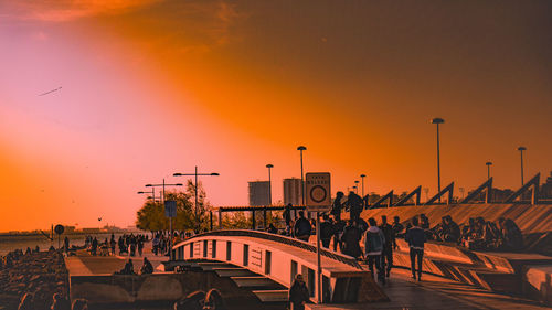 Silhouette people on bridge against orange sky