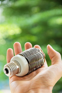 Cropped hand of man holding light bulb against plants