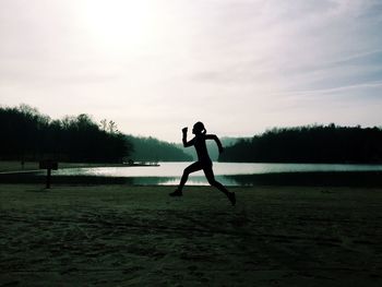 Silhouette woman jogging on grassy field by lake against sky
