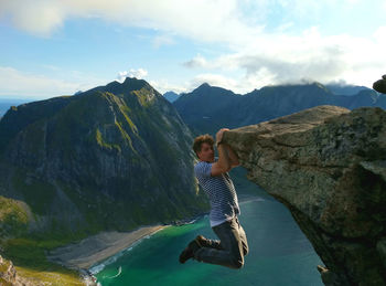 Man hanging on cliff against sky