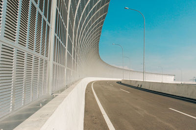 Empty road by bridge against sky in city