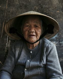 Portrait of senior woman wearing hat sitting against wall