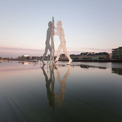 Sculpture by lake against sky during sunset