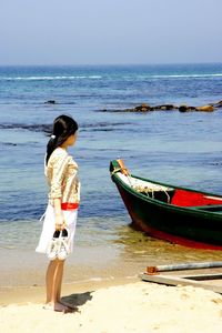 Full length of woman holding shoes on shore at beach