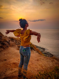 Woman with arms outstretched standing by sea against sky during sunset