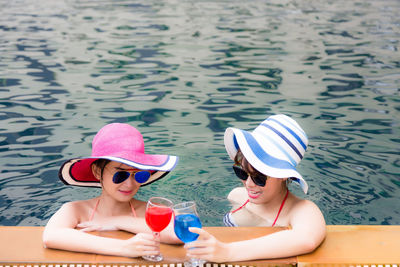 Female friends toasting juice glasses while resting in swimming pool