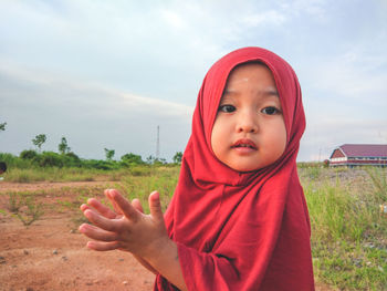 Portrait of cute baby girl in hijab standing on field against sky