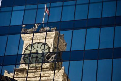 Low angle view of clock tower reflecting on modern building