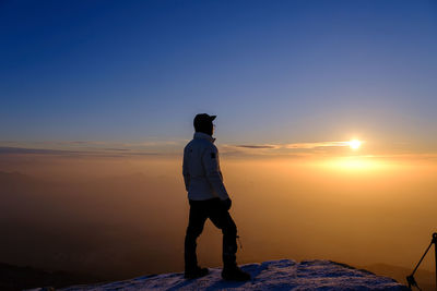 Rear view of man standing on beach against sky during sunset