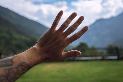 Cropped hand of man gesturing stop sign against mountains