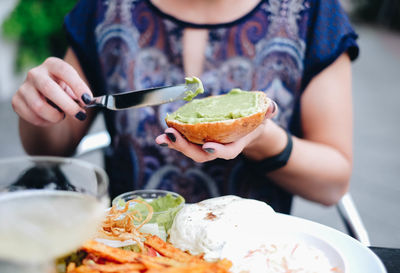 Midsection of woman applying sauce on bun in plate