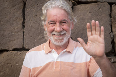 Portrait of smiling senior man standing against wall outdoors