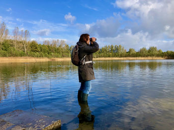 Side view of woman in casual clothes standing with her wellies in a beautiful lake