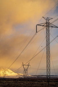 Electricity pylon on land against sky during sunset