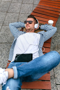 High angle view of young man listening to music while lying on bench