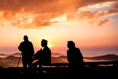 Silhouette people standing against orange sky
