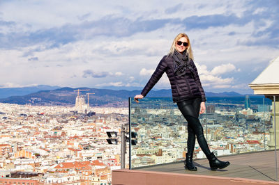 Young woman wearing warm clothing while standing on balcony against cityscape