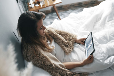 High angle view of woman using digital tablet while sitting on bed