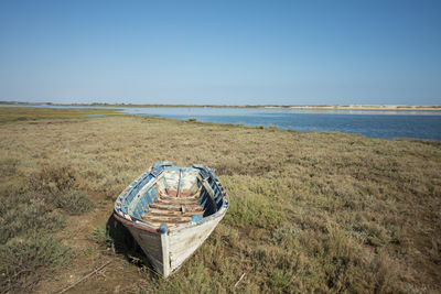 Abandoned rowboat moored on grassy seashore against clear blue sky