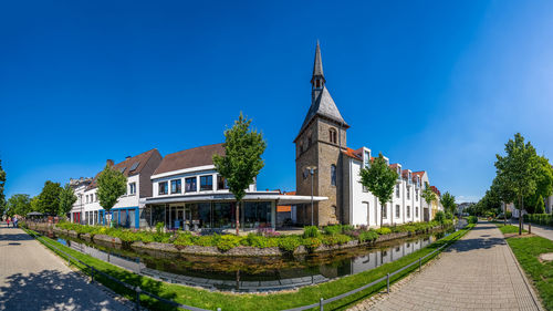 Footpath amidst buildings against clear blue sky