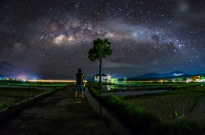 Rear view of woman standing on country road against star field in sky at night