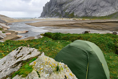 Green tent on a green grass hill at bunes beach with a view over the valley in lofoten norway.