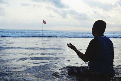 Man sitting on shore at beach against sky