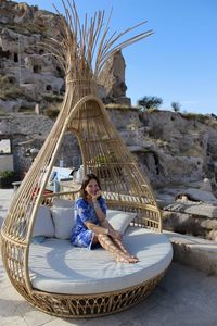 Portrait of happy woman sitting on bamboo sun lounger against blue sky