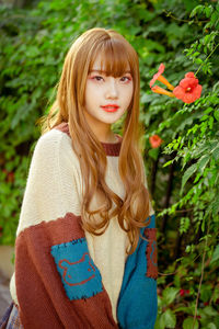 Portrait of beautiful young woman standing by plant