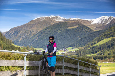 Portrait of woman standing with bicycle by railing against mountains