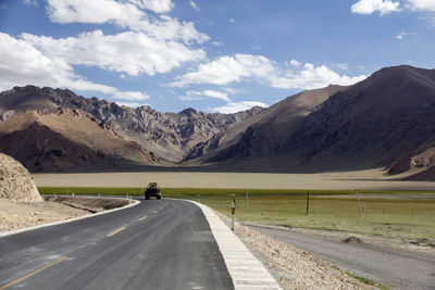A flat, newly built wide asphalt road leads to the beautiful mountains in the distance