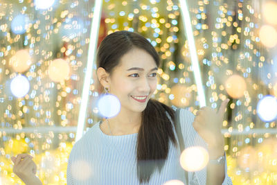 Smiling young woman by illuminated decorative lights at night