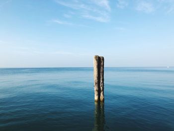 Wooden posts in sea against sky