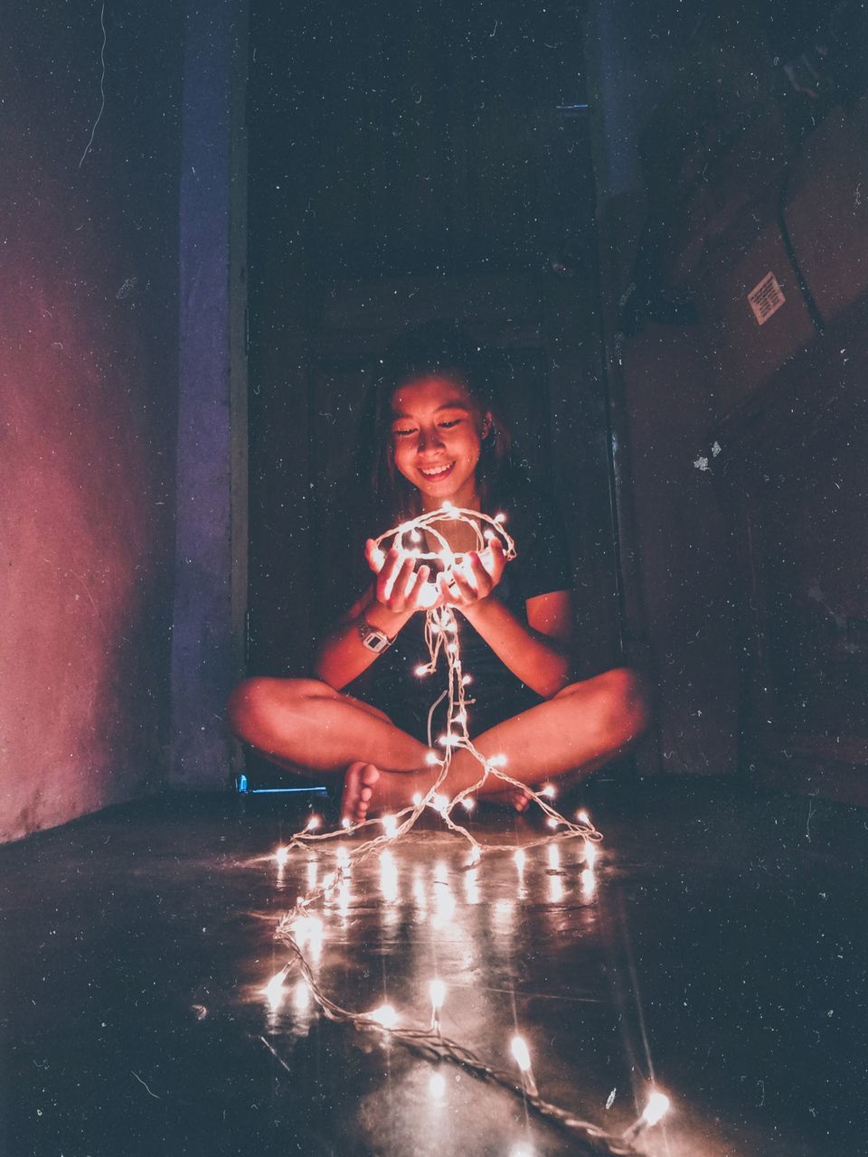 PORTRAIT OF A SMILING YOUNG WOMAN SITTING IN ILLUMINATED ROOM