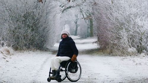 Woman on wheelchair over snow covered road amidst bare trees