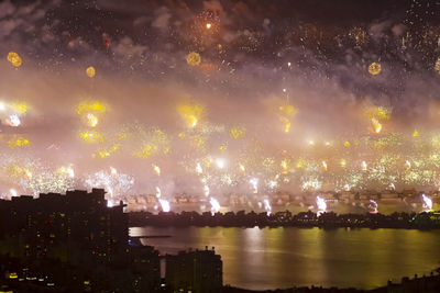 Firework display over river against sky in city at night