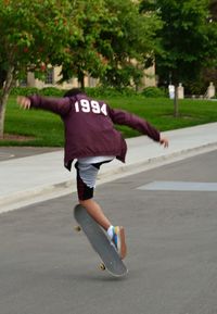 Full length of boy performing stunt with skateboard at street