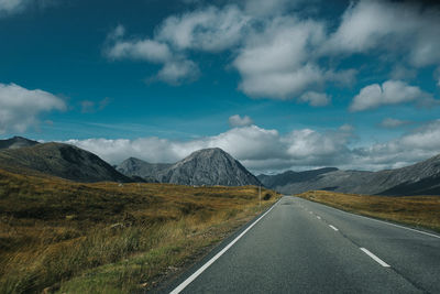 Empty road leading towards mountains against cloudy sky