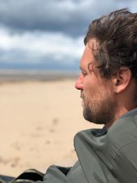 Close-up of man looking away on beach against sky