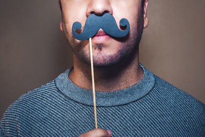 Close-up of man with prop mustache against gray background