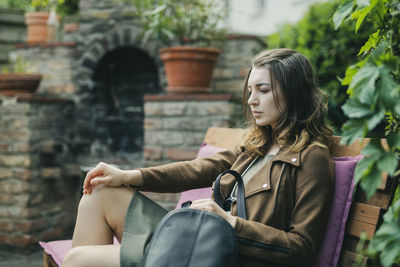 Side view of thoughtful beautiful woman sitting on bench