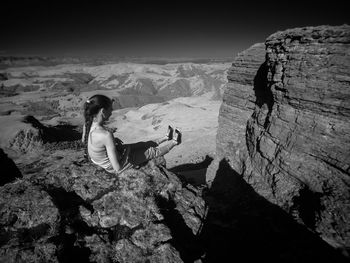 Young woman sitting on rock formation against sky