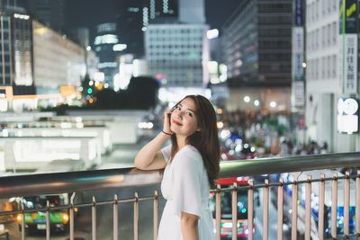 Woman standing by railing in city at night