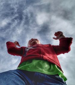 Low angle view of man with red umbrella against cloudy sky