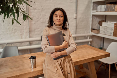 Portrait of smiling woman holding book standing at cafe