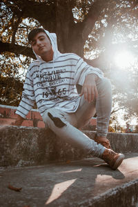 Low angle portrait of young man sitting against tree