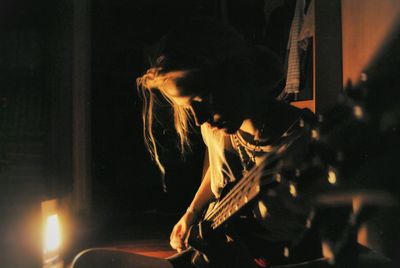 Woman playing guitar while sitting in darkroom